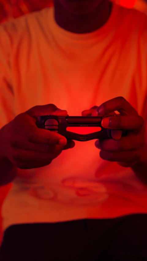 a man holding a video game controller in his hands, pexels, gradient light red, ( ( dark skin ) ), orange neon, low quality photo