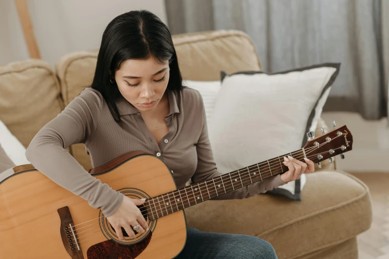 a woman sitting on a couch playing a guitar, pexels contest winner, half asian, helpful, slightly tanned, half length