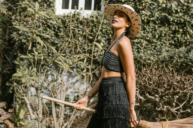 a woman in a straw hat holding a broom, unsplash, wearing crop top, freida pinto, wearing black vest and skirt, garden