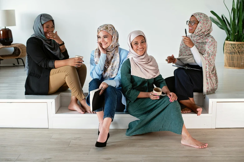 a group of women sitting on top of a white bench, trending on pexels, hurufiyya, wearing a head scarf, sitting on the floor, caucasian, on a desk