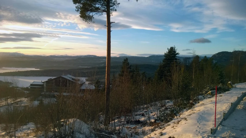 a man riding a snowboard down a snow covered slope, by Anton Lehmden, unsplash, overlooking a valley with trees, sunset panorama, swedish forest, distant mountains lights photo