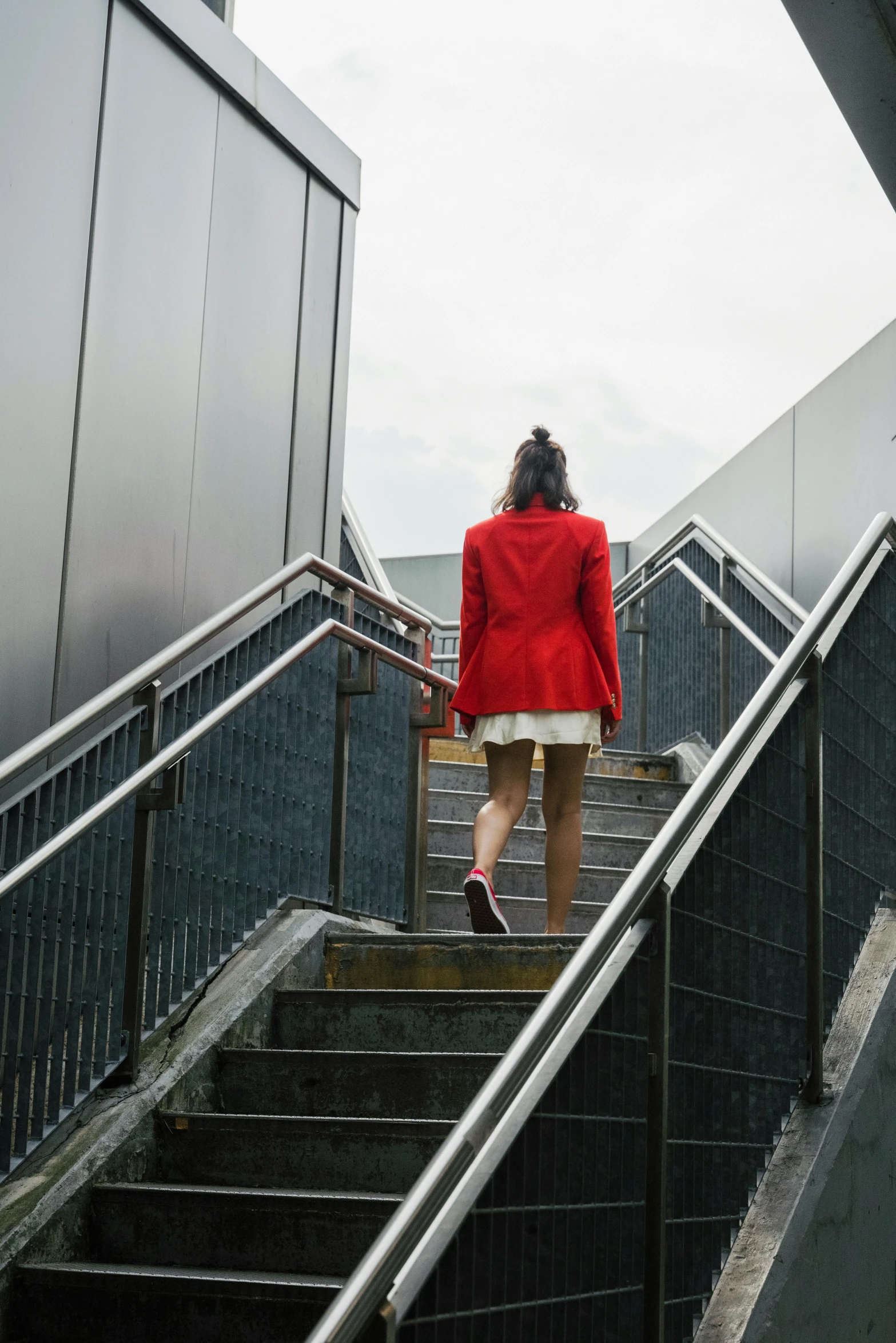 a woman in a red coat walking up a flight of stairs, trending on unsplash, extremely uncomfortable, platforms, back turned, lgbtq