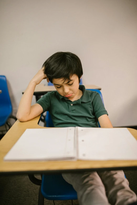 a young boy sitting at a desk in a classroom, by Carey Morris, pexels, sleepy expression, plain background, ignant, reading