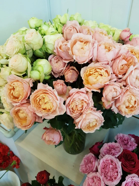 a bunch of flowers in a vase on a table, in shades of peach, rumble roses, persian princess, various sizes