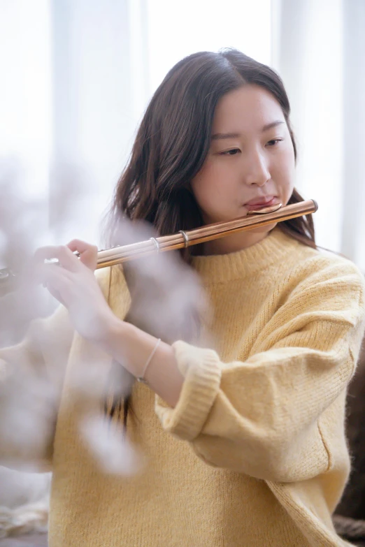 a woman in a yellow sweater playing a flute, inspired by Zheng Xie, trending on pexels, gentle smoke effect, made of bamboo, 4l, jaeyeon nam