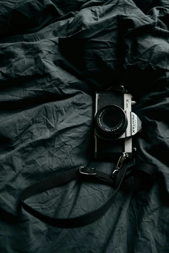 a camera sitting on top of a bed covered in black sheets, by Adam Marczyński, unsplash contest winner, grey backdrop, vintage film stock, wrapped in black, looking up at camera