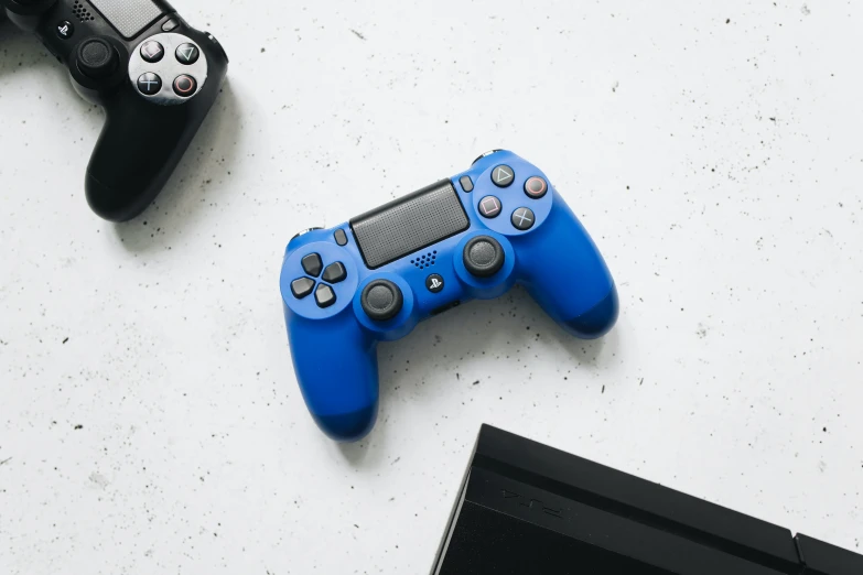 a couple of video game controllers sitting next to a laptop, unsplash, minimalism, electric blue, playstation 4, on a white table, wearing blue