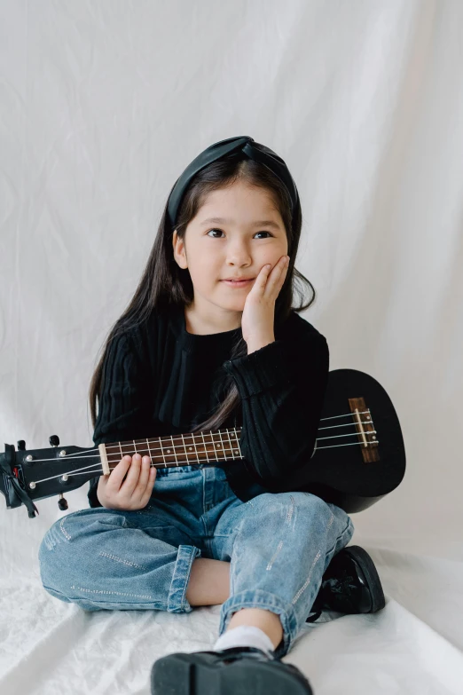 a little girl sitting on a bed holding a guitar, pexels contest winner, plain background, asian female, small chin, greta thunberg