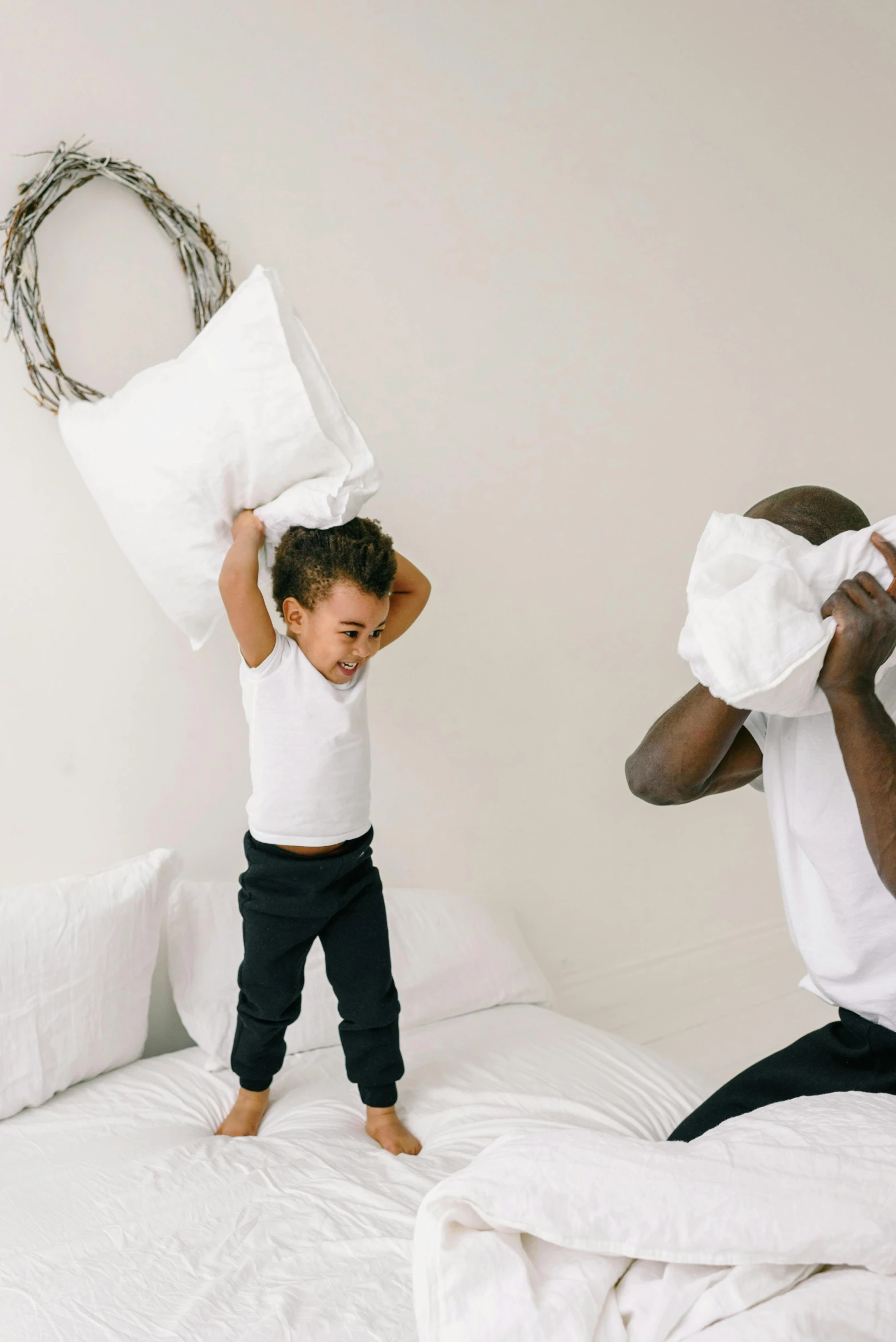 a man and a little boy playing on a bed, white pillows, screaming into air, unbothered, black man