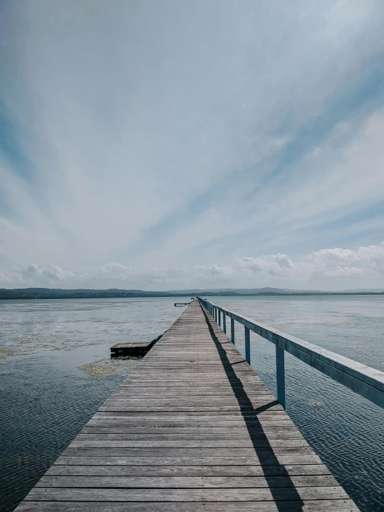 a dock in the middle of a body of water, by Matthias Stom, unsplash, walking to the right, lachlan bailey, colour photograph, long view