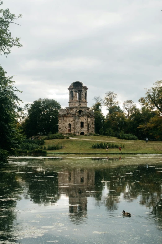 a body of water with a clock tower in the background, baroque, mausoleum tall ruins, lush surroundings, mirrored, mystical kew gardens