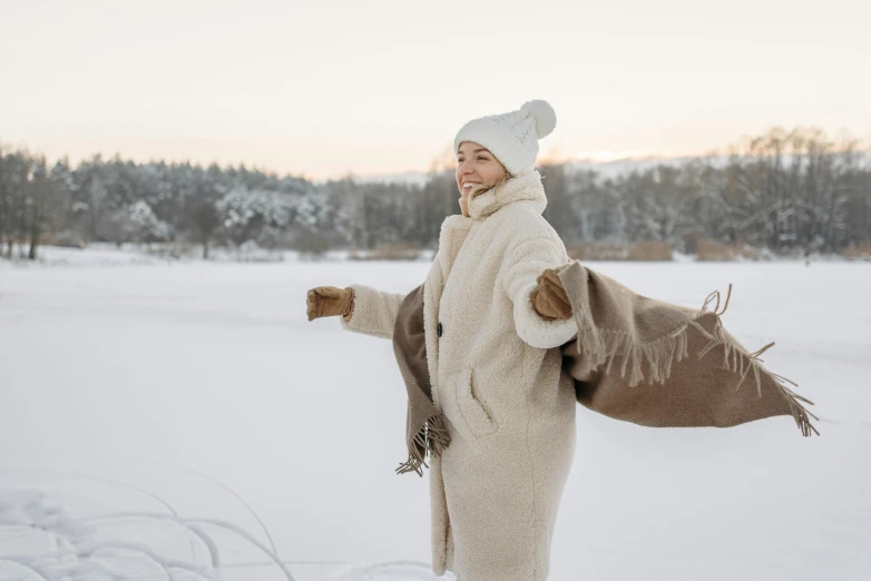 a woman standing on top of a snow covered field, hygge, light tan, thumbnail, wearing a long coat