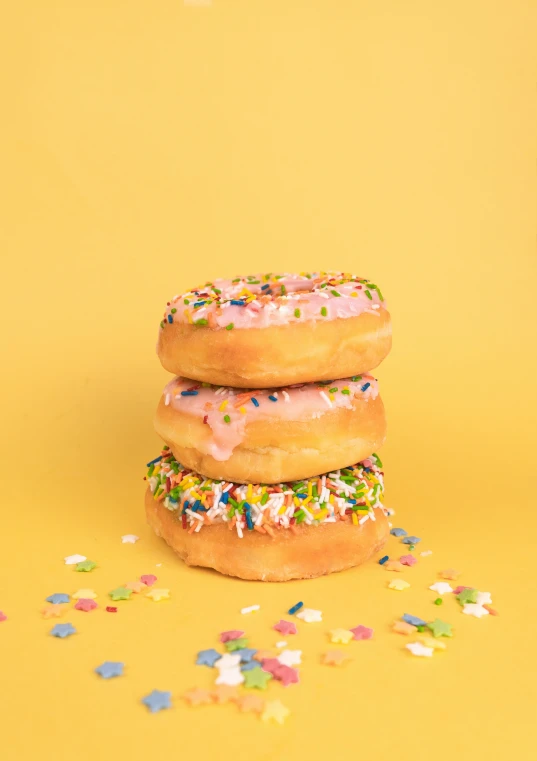 three donuts with sprinkles on a yellow background, a portrait, pexels, stacked, ground broken, tall, neon pastel
