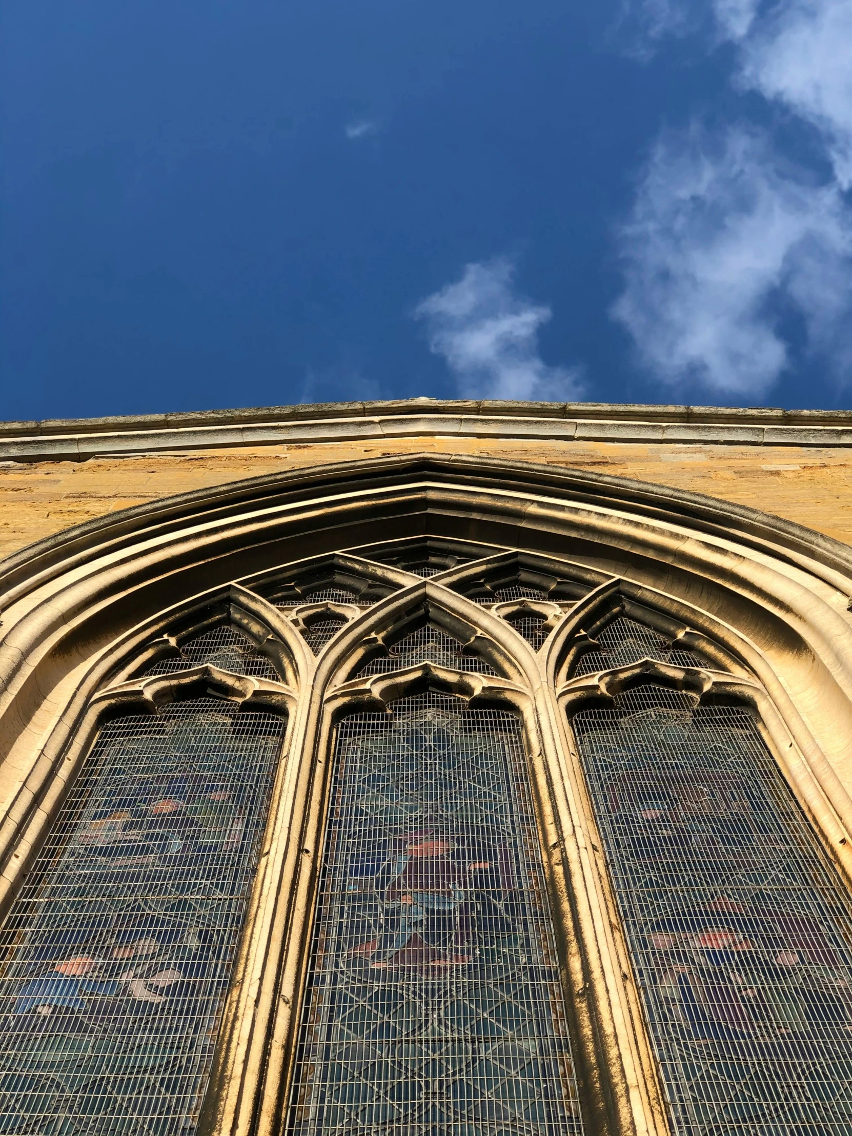 a church window with a blue sky in the background, vibrant but dreary gold, inspiring gothic architecture, etched inscriptions, looking upwards