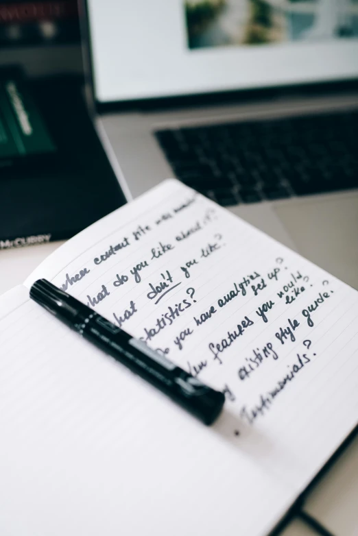 a notepad sitting on top of a desk next to a laptop computer, by Robbie Trevino, unsplash, letterism, black marker, thumbnail, multiple stories, fashionable