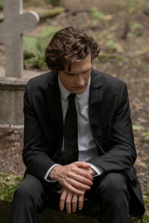 a man in a suit sitting on a grave, an album cover, by Winona Nelson, renaissance, will graham, thick jawline, praying, ( ( theatrical ) )