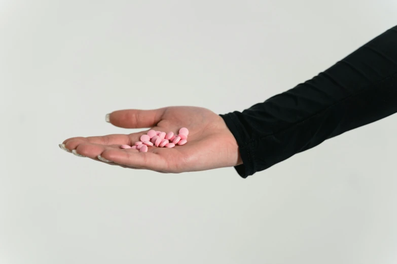 a person holding pink pills in their hand, by Emma Andijewska, antipodeans, licorice allsort filling, modeled, unreleased, 3 4 5 3 1