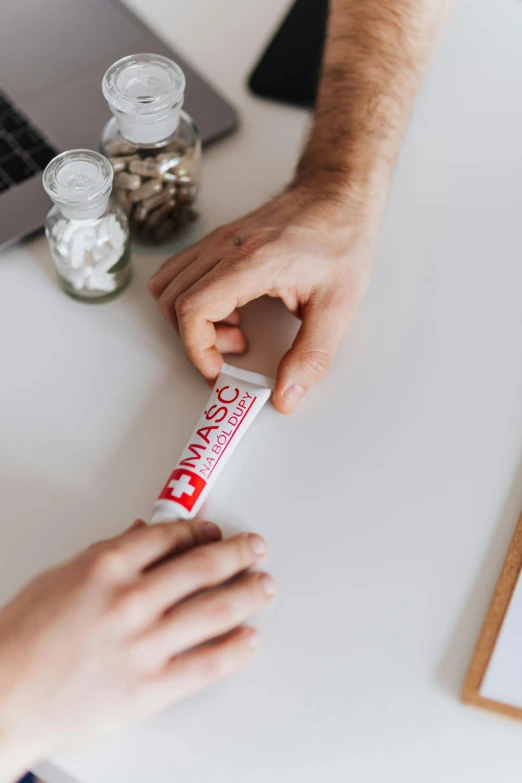 a couple of people that are sitting at a table, holding a syringe, product label, on a wooden desk, supportive