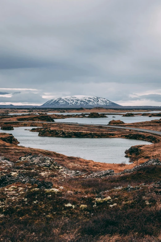 a body of water sitting on top of a grass covered field, by Sebastian Spreng, trending on unsplash, land art, ice mountains in the background, scattered islands, high quality photo, in the distance is a rocky hill