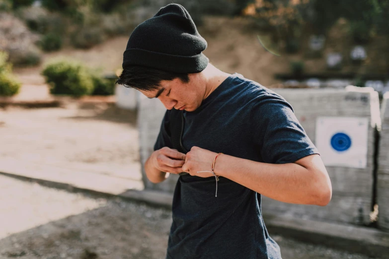 a man looking down at his cell phone, by Ryan Pancoast, pexels contest winner, wearing a tee shirt and combats, holding a magic needle, outdoors, black beanie