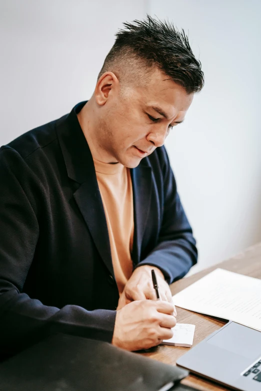 a man sitting at a desk in front of a laptop, inspired by Carlos Berlanga, pexels contest winner, pen and paper, till lindemann, damien tran, writing on a clipboard
