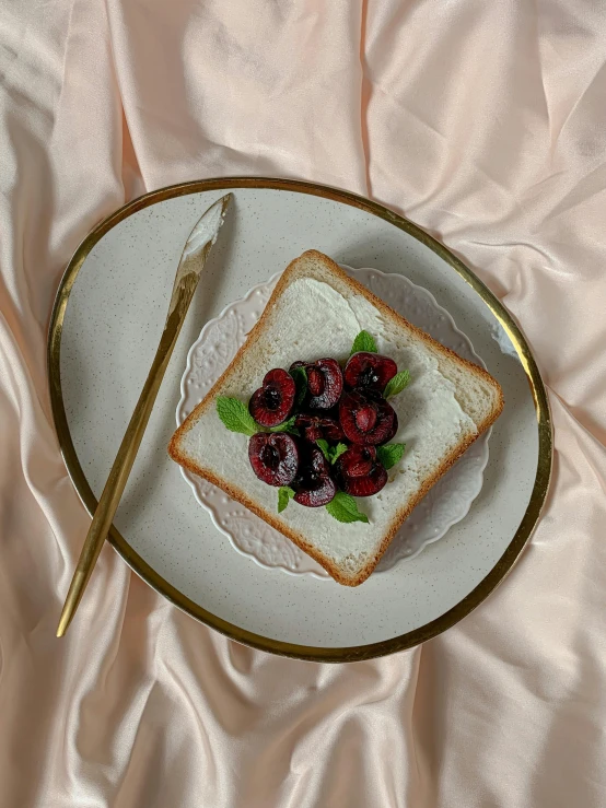 a white plate topped with a piece of bread next to a fork, a still life, inspired by Richmond Barthé, unsplash, cherries, chie yoshii, velvet tablecloth, 2 5 6 x 2 5 6 pixels