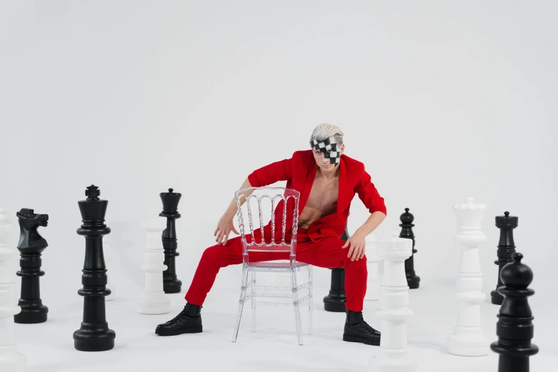 a man sitting on a chair surrounded by chess pieces, an album cover, inspired by Horace Vernet, pexels contest winner, red jumpsuit, xqc, zentai suit, youtube thumbnail