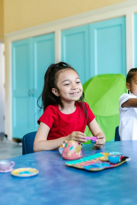 a couple of kids that are sitting at a table, profile image, thumbnail, she is smiling and excited, person in foreground