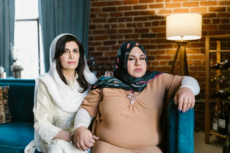 two women sitting next to each other on a couch, hurufiyya, controversial, portrait image, modest, full-figure
