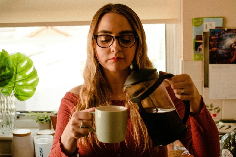 a woman is pouring a cup of coffee, a portrait, by Joe Bowler, pexels, wearing black frame glasses, annoyed, sydney sweeney, justina blakeney