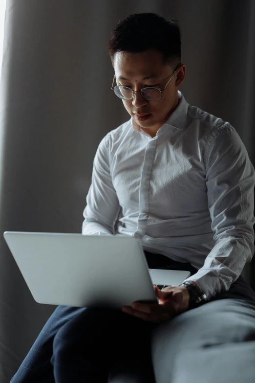 a man sitting on a couch using a laptop computer, inspired by Fei Danxu, trending on unsplash, renaissance, wearing white suit and glasses, serious lighting, wearing a white button up shirt, avatar image