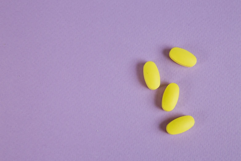 a couple of yellow pills sitting on top of a purple surface, trending on pexels, antipodeans, pastel neon, tinnitus, hivis, a wooden