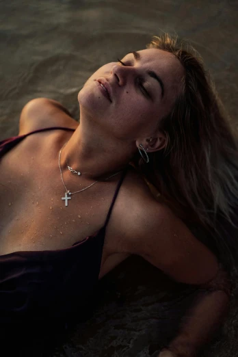 a beautiful woman laying on top of a sandy beach, inspired by Elsa Bleda, trending on pexels, renaissance, beads cross onbare chest, glowing with silver light, portrait shot 8 k, tanned