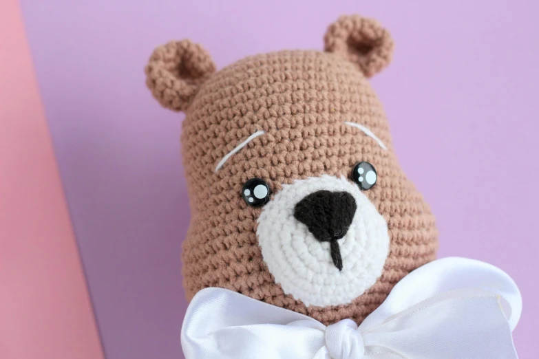 a crocheted teddy bear with a white bow tie, inspired by Károly Brocky, hurufiyya, face detail, blushing, brown, product shot