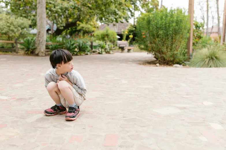 a young boy sitting on top of a skateboard, by Winona Nelson, pexels, disappointed, in garden, stand on stone floor, they are crouching