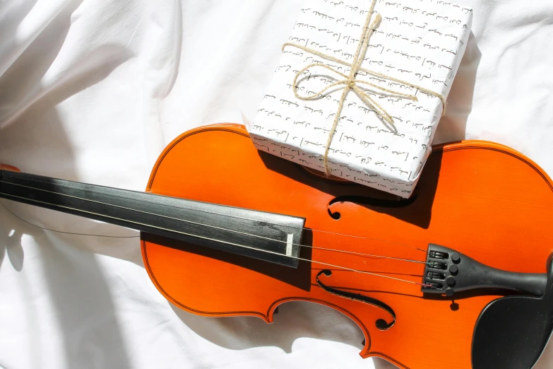 an orange violin sitting on top of a white sheet, pexels contest winner, giving gifts to people, rectangle, white, 🦩🪐🐞👩🏻🦳