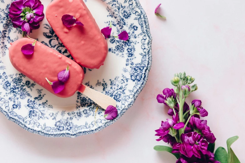 two pops sitting on top of a blue and white plate, inspired by Richmond Barthé, pexels contest winner, romanticism, pink petals fly, strawberry ice cream, background image, edible flowers