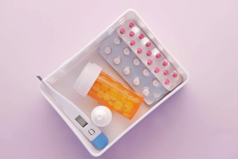a close up of a container of pills and a thermometer, a picture, trending on pexels, electronic case display, good housekeeping, pastel overflow, bottom angle
