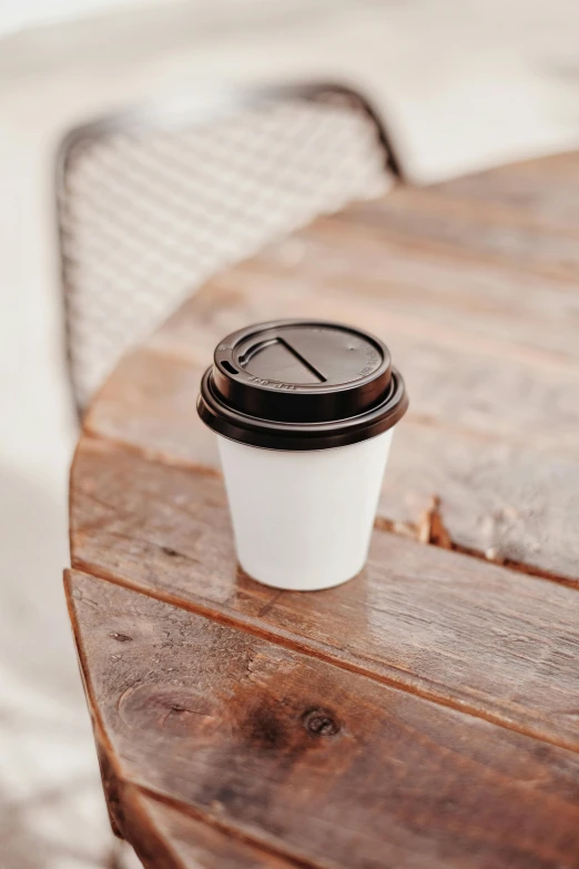 a coffee cup sitting on top of a wooden table, by Nicolette Macnamara, trending on unsplash, paper cup, multiple stories, al fresco, thumbnail