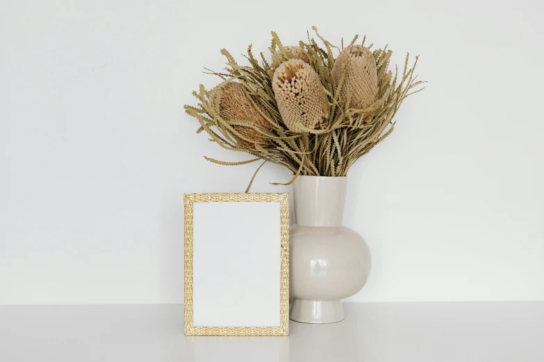 a white vase filled with dry grass next to a picture frame, pexels contest winner, beige color scheme, miniature product photo, background image, metal plate photograph