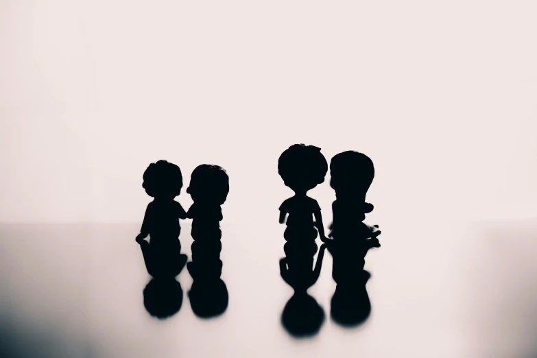 a couple of figurines standing next to each other, a black and white photo, by Lucia Peka, pexels contest winner, minimalism, children's toy, detailed silhouette, three heads, holding each other