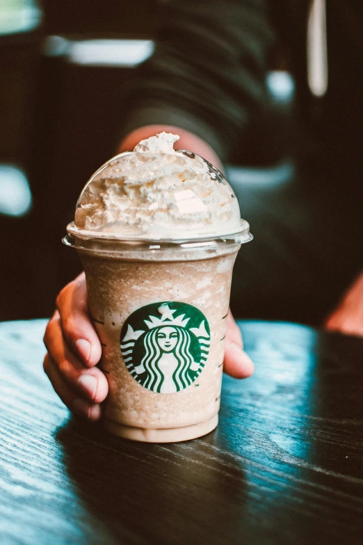 a person holding a cup of coffee on a table, starbucks, whipped cream, slush, brown mist