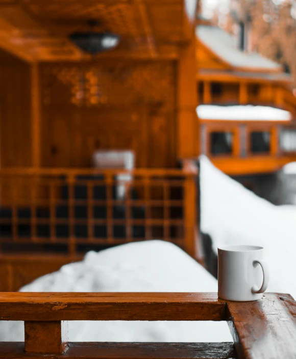 a cup of coffee sitting on top of a wooden table, by Julia Pishtar, pexels contest winner, snow outside the windows, thumbnail, multiple stories, chalet