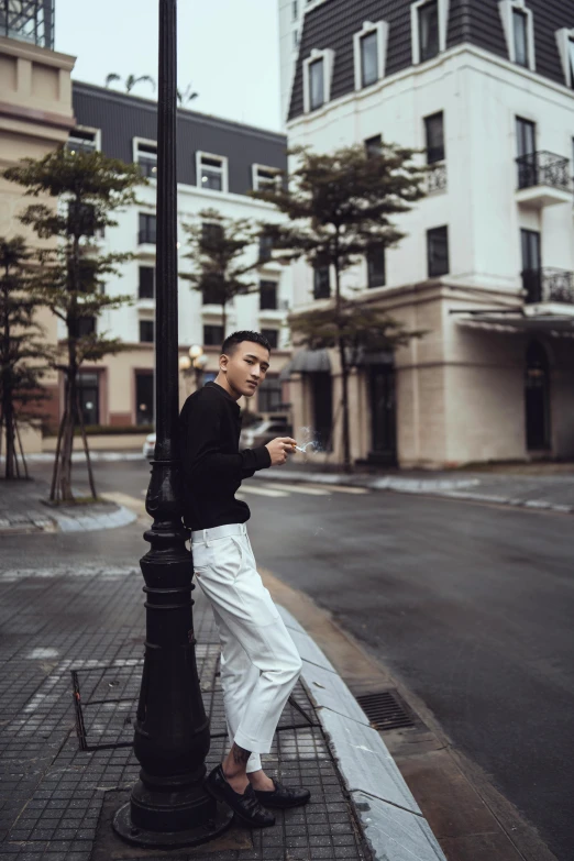 a man standing on a sidewalk next to a lamp post, by Cheng Jiasui, trending on unsplash, happening, white pants, drinking a coffee, striking a pose, cai xukun