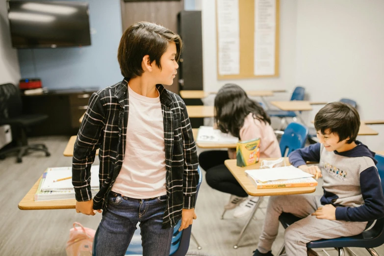 a group of children sitting at desks in a classroom, a picture, by Byron Galvez, pexels contest winner, american barbizon school, a person standing in front of a, getting ready to fight, looking to his side, meg kimura