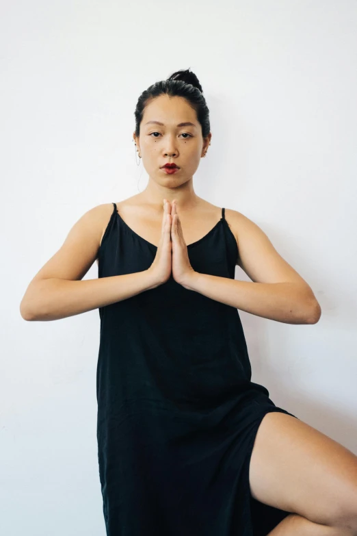 a woman in a black dress doing a yoga pose, inspired by Kim Tschang Yeul, looking towards camera, hand gesture, jen yoon, black