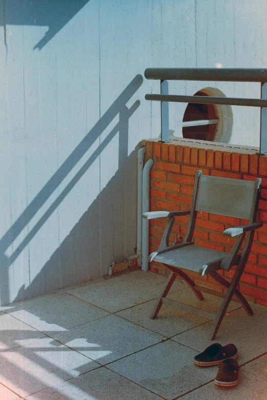 a chair sitting on top of a tiled floor next to a brick wall, an album cover, inspired by Louis Stettner, unsplash, photorealism, blocking the sun, balcony, clemens ascher, revolver on chair