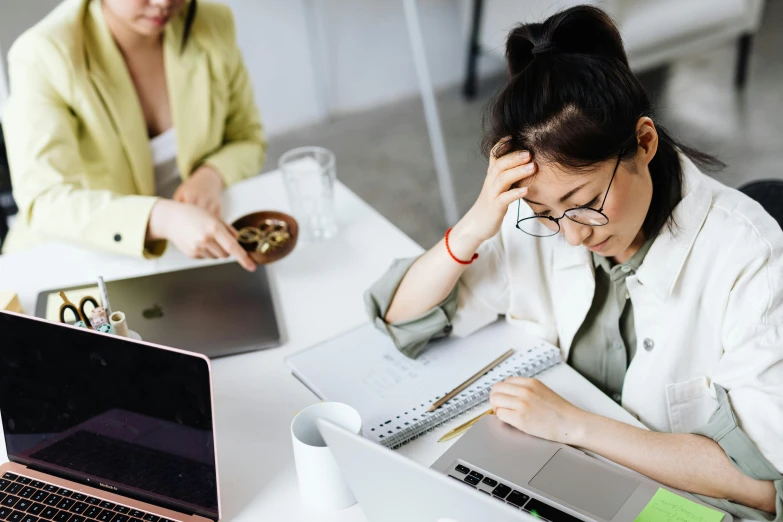 a couple of women sitting at a table with laptops, a cartoon, trending on pexels, looking exhausted, an asian woman, professional photo, sprawling