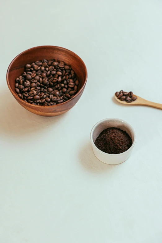 a bowl of coffee beans next to a wooden spoon, detailed product image, hills, curated collection, powder