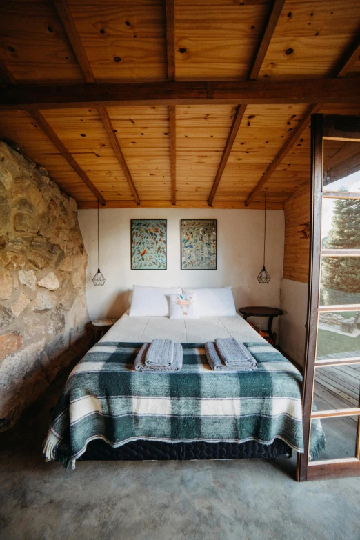 a bed sitting inside of a bedroom next to a window, by Jessie Algie, unsplash, patagonian, stone roof, pine treehouse, full frame image